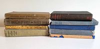 Full lot showing two stacks of eight antique schoolbooks