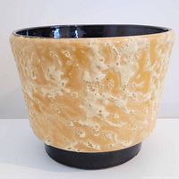 Side view of beige crater glazed planter with black foot