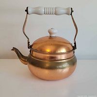Full view of copper finished kettle with handle up and lid on