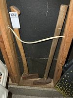 Full view of both wood handled axes leaning against wall