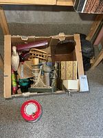 Overview of box showing candlestick holder, pottery bank, wooden items, tin