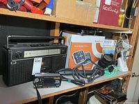 Shelf with large vintage radio, crank radio, Philips DVD player box, VTech phone, neck comforter box, cordless screwdriver