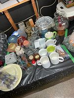 Overview of assorted candle holders, mugs, plastic plates, bath set and more on table