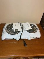 Front angled view of Salton double burner hotplate with cord and manual on wooden table