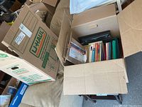 Two open U-Haul boxes showing assorted file folders, binders and office supplies