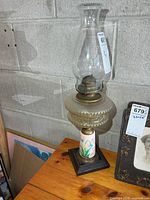 Full view of antique oil lamp on table showing chimney, burner, font, stem, base