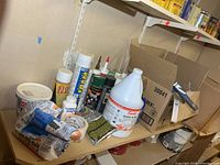 Overall shelf view with assorted caulks, cleaner jug, paint accessories