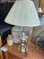Full view of brass table lamp with pleated shade on wooden surface