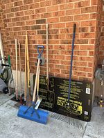 Line-up of all long-handled yard tools and KwicKan insert against brick wall