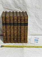 Front view of all seven matching leather bound volumes with tape measure for scale