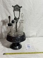 full view of cruet set showing stand, bottles, spoon, measuring tape for scale