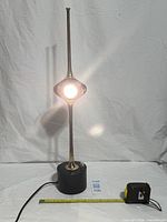 Front view of brass Cobra lamp illuminated, showing black base, brass stem, globe shade, power adapter