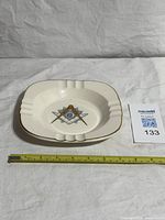 Top view showing ashtray shape, emblem, and ruler for scale