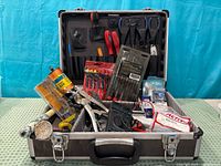 Open metal tool case showing multimeter, pliers, screwdrivers and packaged items