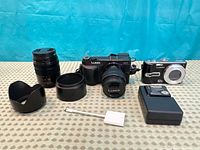 Entire lot laid out showing GX7 with lens, 45-150 mm lens, TZ3 camera, two lens hoods, charger, adapter