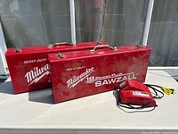 Two red Milwaukee Sawzall cases and fast charger on table