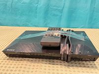 Front view of Sony Blu-ray player with remote taped on top and power cord bundled