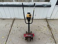 Front view of cultivator showing handlebars, engine, tines and branding