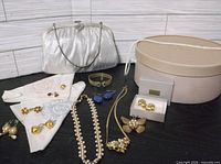 Group shot of evening bag, hat box, hankies and assorted jewelry displayed