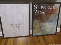 Two packaged Supreme Wood poster frames standing on floor