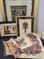 Group view of framed and loose papyrus paintings with leather panel