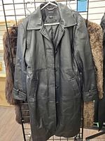 Front view of black leather coat hanging, showing button front and collar