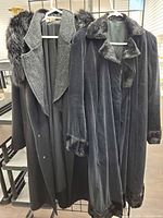 Two long coats hanging, showing overall design and fur trims