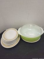 Stack of eight Royal Doulton plates beside green Pyrex casserole with lid