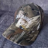 Three-quarter view of the camouflage cap showing front logo and brim