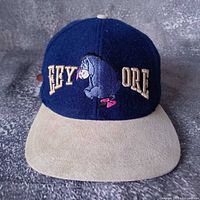 Front view of blue felt hat with beige brim and embroidered Eeyore logo