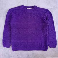 Full front view of purple cable-knit sweater laid flat