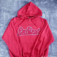 Full front view of red hoodie with hood up showing kangaroo pocket and chest logo