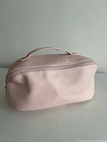 Front view of blush pink cosmetic bag showing soft exterior and top handle