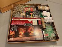 Box containing multiple packaged and loose LED fairy lights, visible Sylvania box and spooled strands