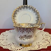 Front view of teacup with saucer showing gold filigree and script
