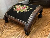 Angled view of footstool showing needlepoint top and frame