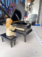 Rear angle showing piano lid open, girl figurine seated at bench and measuring tape for scale