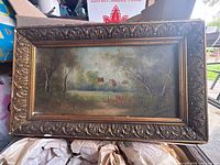 Frontal view of framed oil painting showing landscape scene and gilt frame
