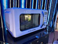 Front angled view of Galanz white countertop microwave on a stand