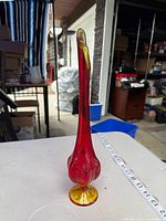 Full view of red and amber bud vase next to measuring tape