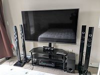 Overall view of LG TV on stand with four tower speakers, soundbar, subwoofer, receiver and remotes