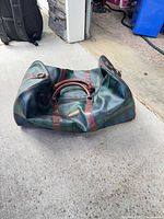 Full view of duffel bag showing plaid pattern, leather handles, overall shape