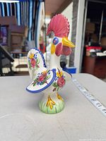 Side view of glazed ceramic rooster showing multicolor floral motifs, red comb, yellow beak, base detail