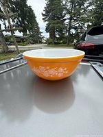 Side view of orange Pyrex bowl with white floral design