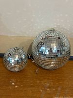 Large and small disco balls side by side on table showing size comparison and hanging cable