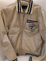 Front view of beige leather Chevignon bomber jacket showing zipper closure, chest patch, ribbed trim