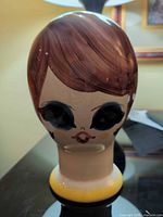 front view of ceramic head vase showing painted face and yellow base rim