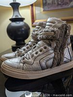 Left side view of both sneakers showing metallic leather, shearling lining, zipper, straps