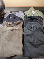 Eight folded garments including sweaters, tops and pants