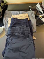 Stack of four pants showing colors grey, khaki, navy, dark navy